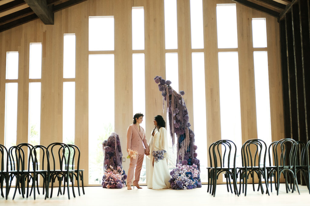 Two brides in front of purple, modern ceremony backdrop