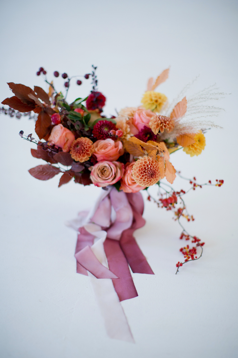 Beautiful autumn bouquet with orange and red flowers and berries. Autumn bouquet with ribbons on a white background